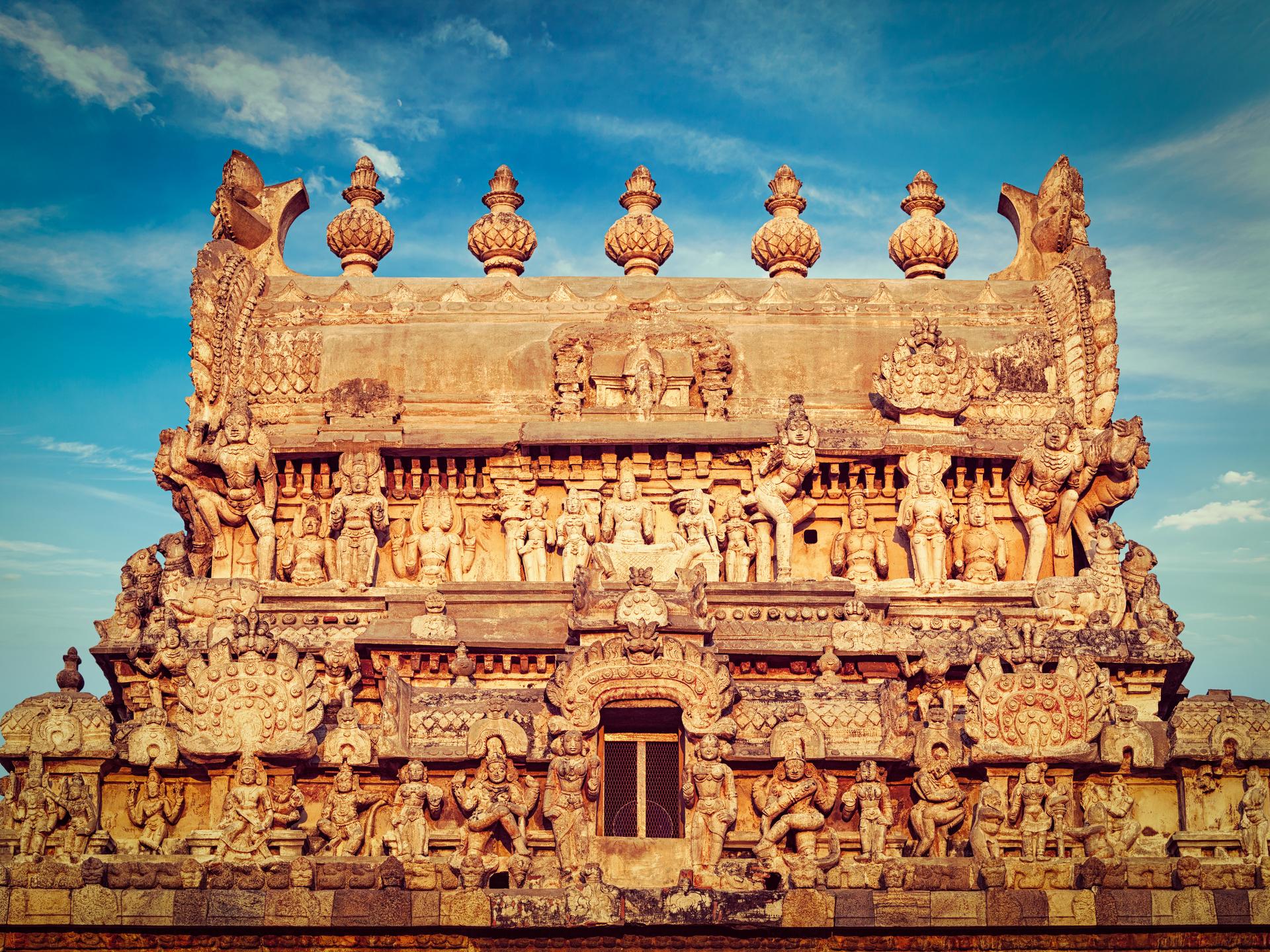 The carved upper tier of a Dravidian gopuram, its kalasha finials against a blue sky.