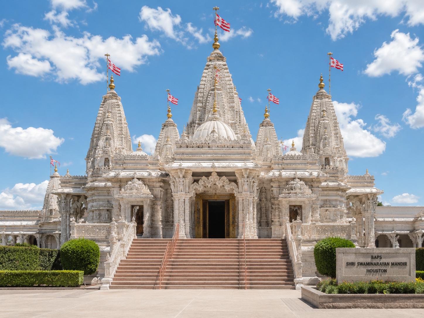 The white-marble BAPS Shri Swaminarayan Mandir, Houston, its carved shikharas beneath a blue sky.