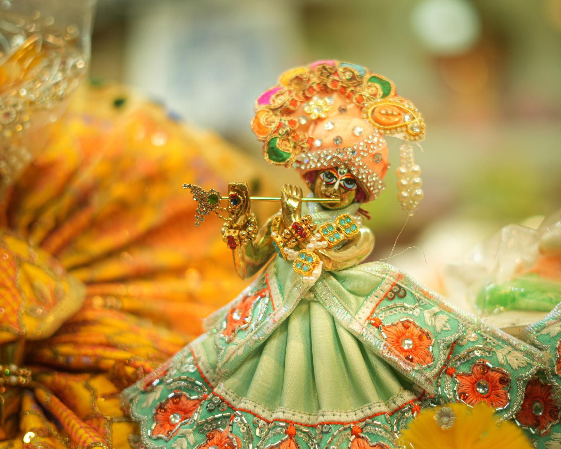 A deity of Krishna adorned in a jeweled green outfit.