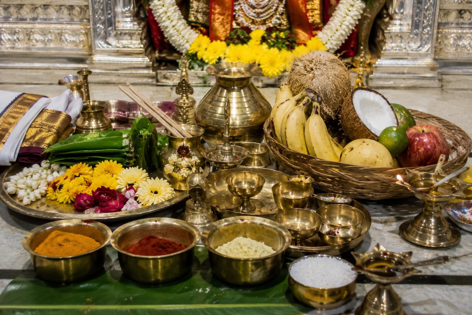Brass puja vessels, fruit, flowers, and kumkum arranged for worship.